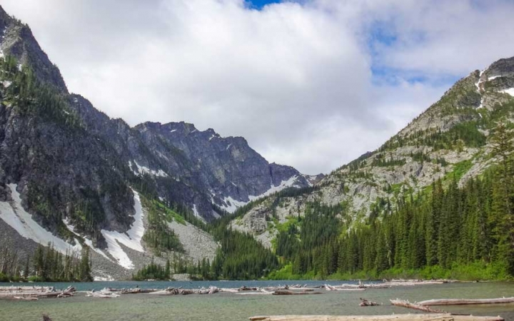 A body of water is framed by mountains, dotted with trees and snow.
